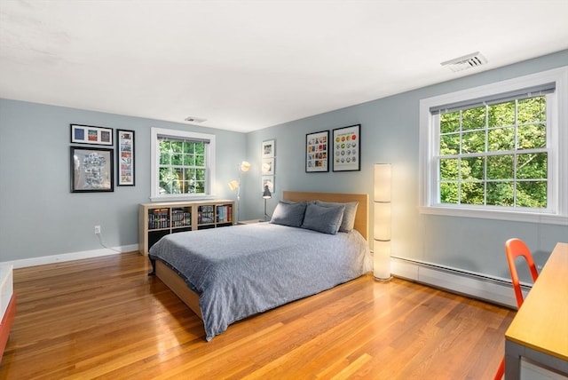 bedroom featuring a baseboard heating unit, baseboards, visible vents, and wood finished floors