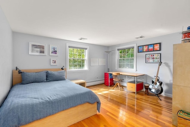 bedroom with baseboard heating, visible vents, and wood finished floors