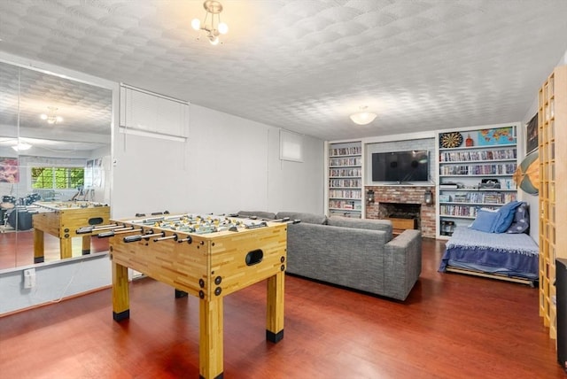 game room with a fireplace, built in shelves, wood finished floors, and a textured ceiling