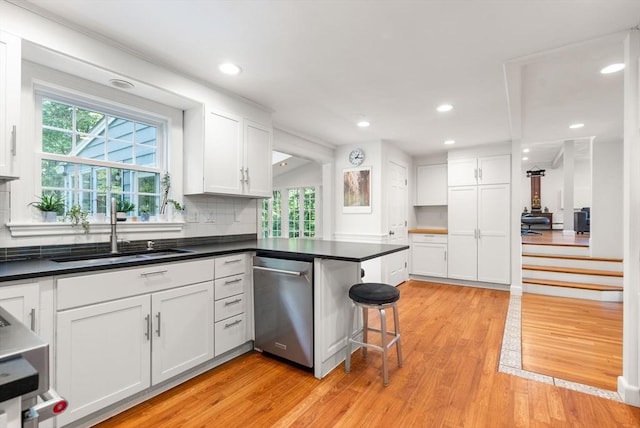 kitchen with light wood-style floors, stainless steel dishwasher, dark countertops, and white cabinetry