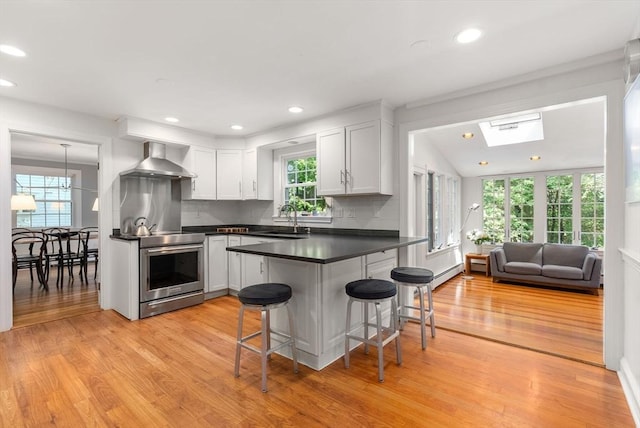 kitchen with dark countertops, wall chimney range hood, a kitchen bar, stainless steel range with electric stovetop, and a sink