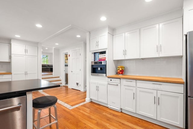 kitchen with tasteful backsplash, a breakfast bar area, light wood-style floors, white cabinets, and stainless steel appliances