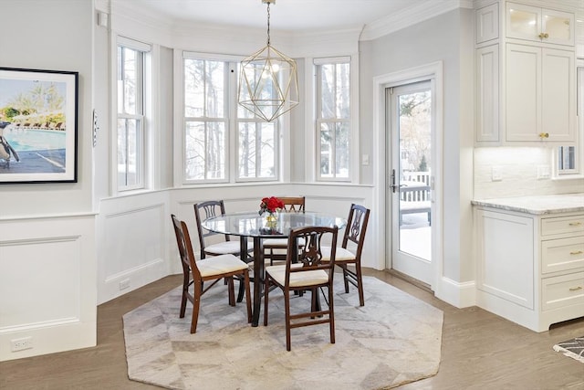 dining space with light wood-type flooring, a notable chandelier, crown molding, and a decorative wall