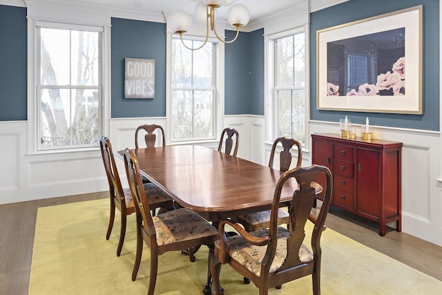 dining room featuring wood finished floors, a wainscoted wall, an inviting chandelier, crown molding, and a decorative wall