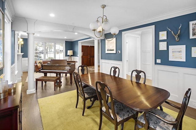 dining area featuring crown molding, a chandelier, decorative columns, wainscoting, and wood finished floors