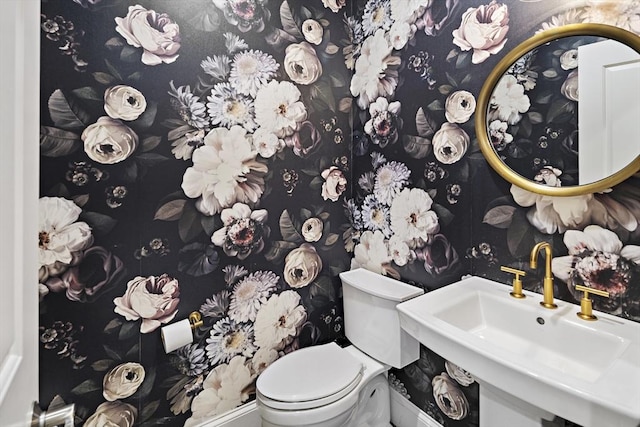 bathroom featuring toilet, wallpapered walls, and a sink