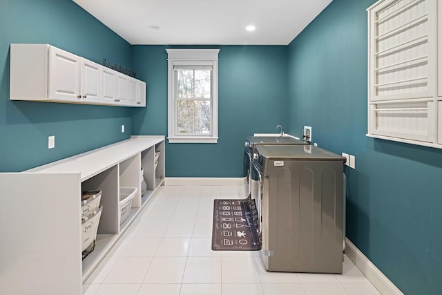 clothes washing area with tile patterned floors, washing machine and dryer, cabinet space, and baseboards