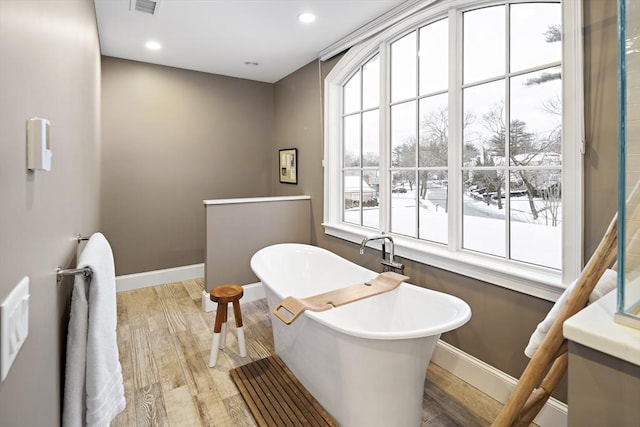 full bathroom with a freestanding tub, plenty of natural light, baseboards, and wood finished floors