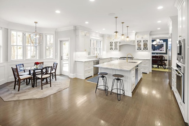 kitchen with an island with sink, dark wood-style flooring, ornamental molding, decorative backsplash, and stainless steel appliances