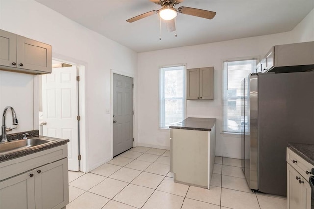 kitchen with dark countertops, light tile patterned floors, freestanding refrigerator, and a sink