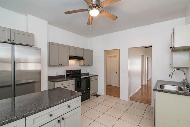 kitchen featuring light tile patterned floors, stainless steel refrigerator, a sink, black range with electric stovetop, and under cabinet range hood