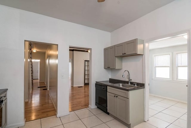 kitchen featuring gray cabinets, a sink, black dishwasher, dark countertops, and light tile patterned floors