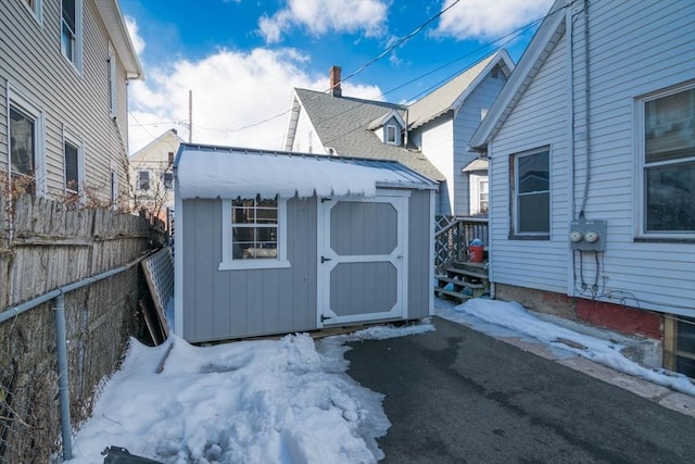 snow covered structure featuring a storage unit, an outdoor structure, and fence