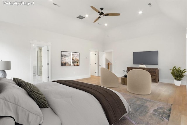 bedroom featuring ceiling fan, ensuite bathroom, light hardwood / wood-style floors, and a towering ceiling