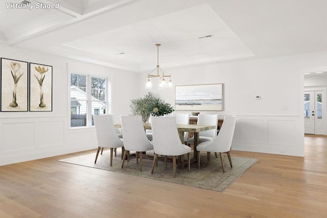 dining area with a raised ceiling, a notable chandelier, and light hardwood / wood-style floors