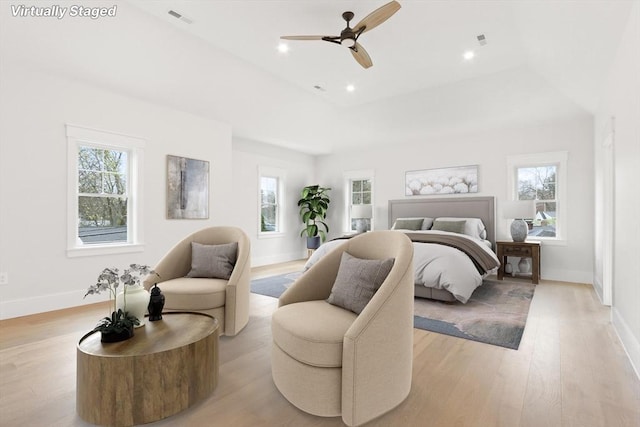 bedroom with ceiling fan, a raised ceiling, light hardwood / wood-style floors, and multiple windows