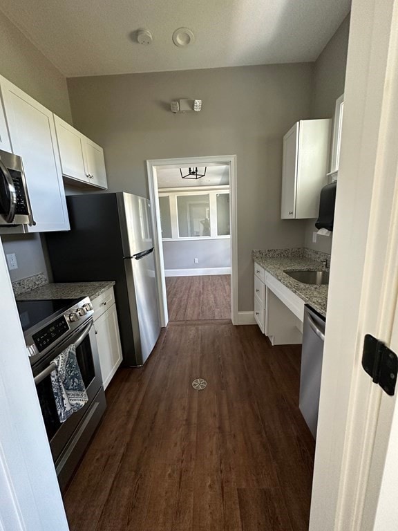 kitchen with stainless steel appliances, white cabinetry, light stone countertops, dark wood-type flooring, and sink