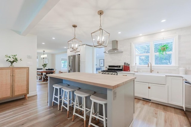 29 Regal St, Holliston, MA 01746 - kitchen featuring wall chimney range hood, stainless steel appliances, a sink, light wood finished floors, and a kitchen island
