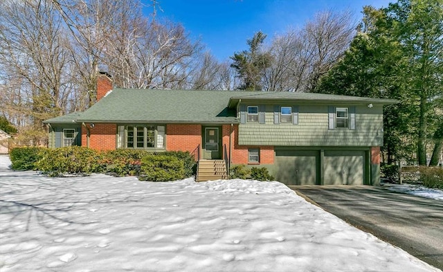 split level home with aphalt driveway, brick siding, a chimney, and a garage