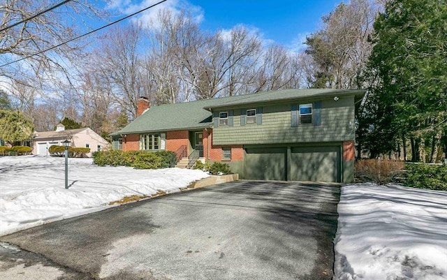 split level home with aphalt driveway, brick siding, and a chimney