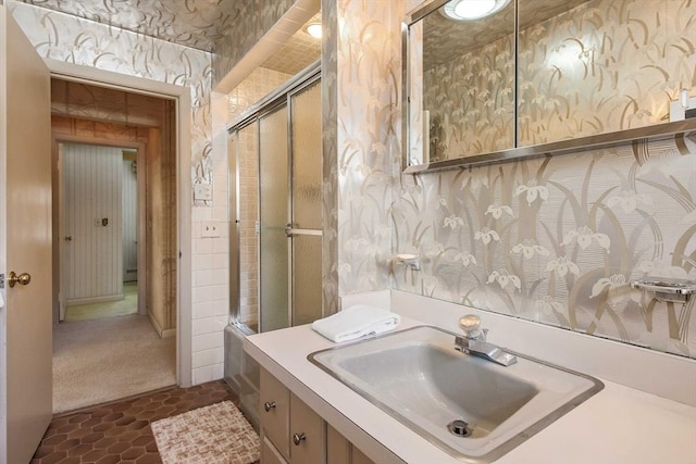 full bath featuring vanity, a shower with door, and wallpapered walls