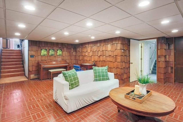 living area featuring brick floor, a baseboard radiator, recessed lighting, wood walls, and stairs