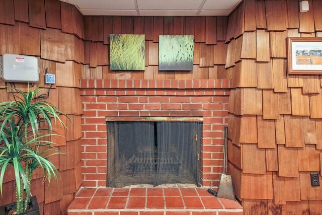 interior details with a brick fireplace, a drop ceiling, and wooden walls