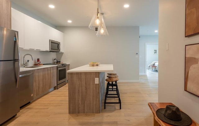 kitchen featuring pendant lighting, appliances with stainless steel finishes, a kitchen island, white cabinetry, and light wood-type flooring