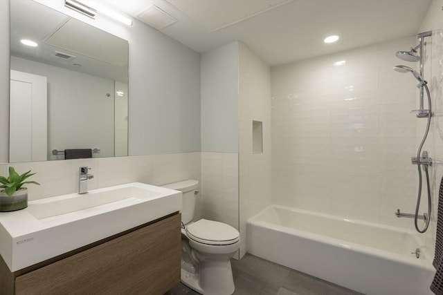 full bathroom featuring toilet, tile walls, tiled shower / bath, and vanity