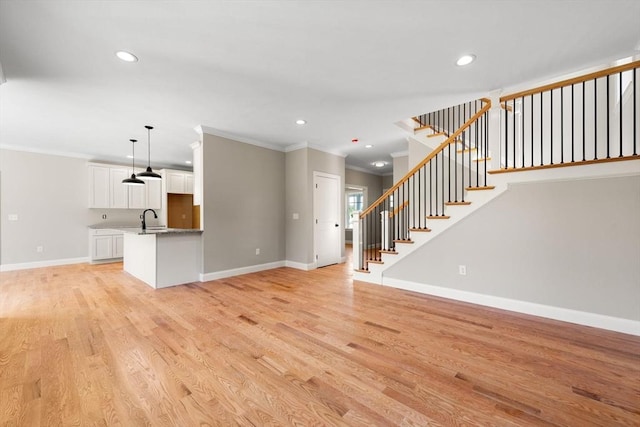 unfurnished living room with ornamental molding, sink, and light hardwood / wood-style floors