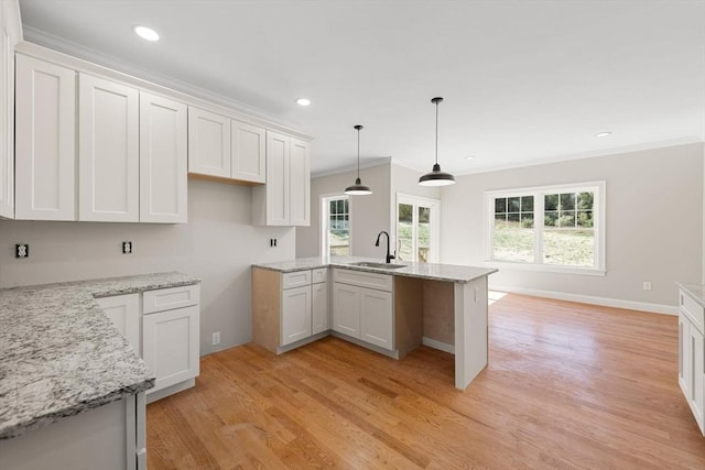 kitchen with white cabinetry, sink, hanging light fixtures, and light wood-type flooring