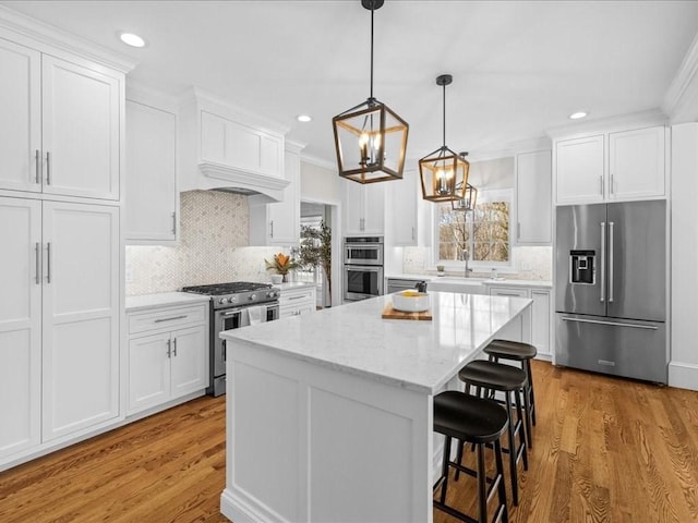 kitchen with light stone counters, hanging light fixtures, premium appliances, a kitchen island, and white cabinets