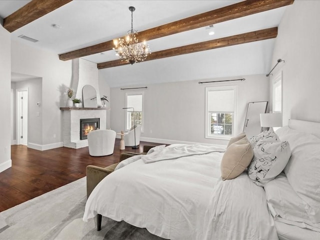 bedroom featuring beamed ceiling, wood-type flooring, a chandelier, and a fireplace