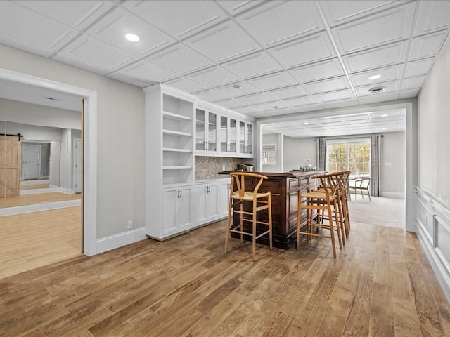 bar featuring light hardwood / wood-style flooring, a barn door, and white cabinets