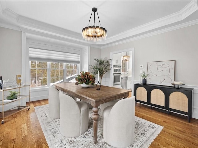 dining space with crown molding, light hardwood / wood-style floors, a chandelier, and a tray ceiling