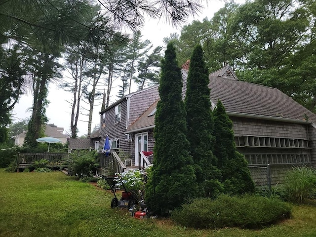 view of side of home with a shingled roof, a yard, and a deck