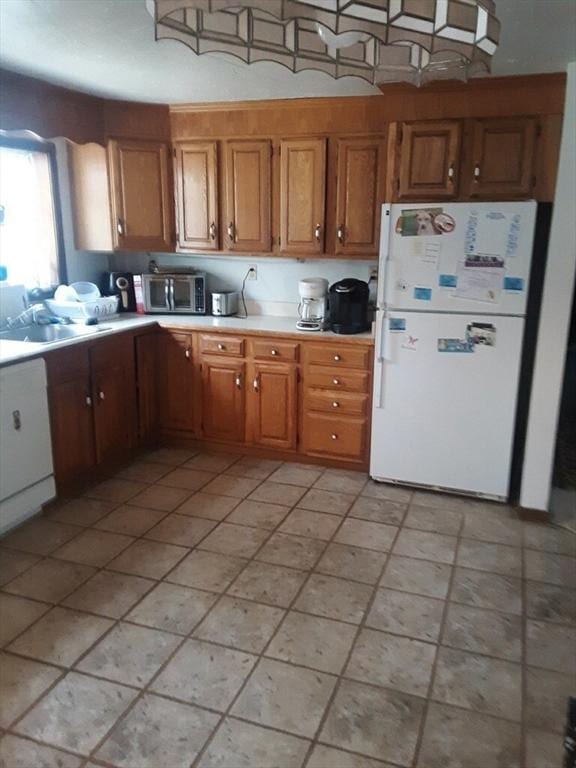 kitchen featuring brown cabinetry, freestanding refrigerator, light countertops, and stainless steel microwave