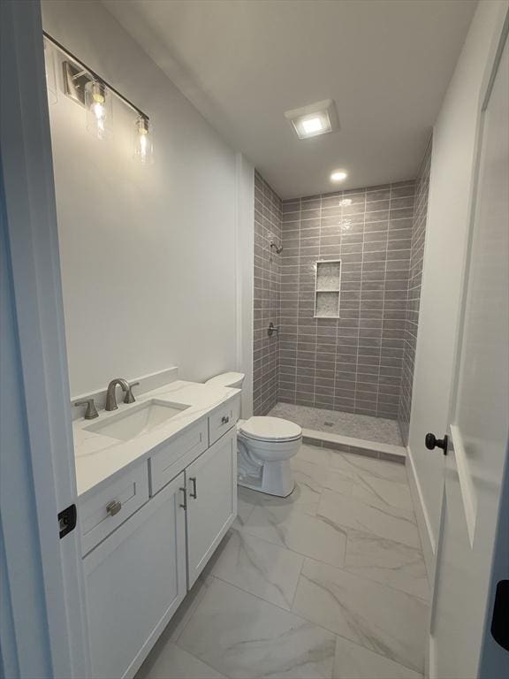 bathroom featuring toilet, a tile shower, and vanity