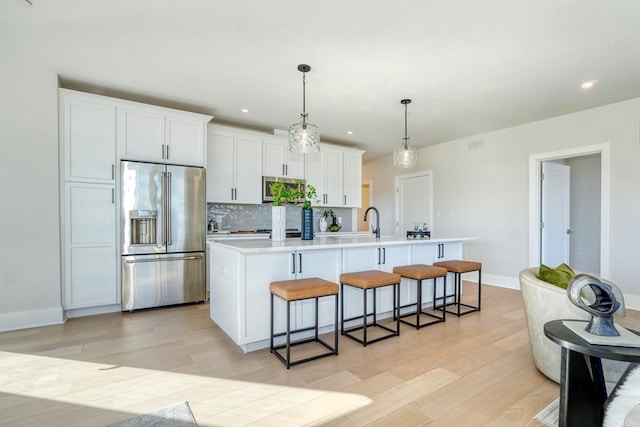 kitchen featuring stainless steel appliances, backsplash, a kitchen island with sink, pendant lighting, and white cabinets