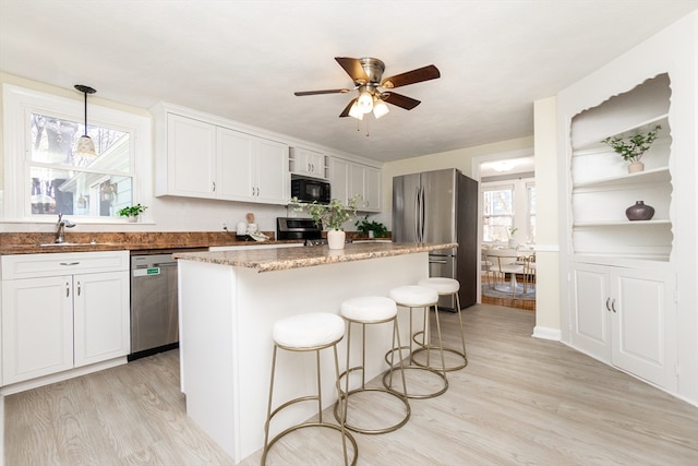 kitchen featuring white cabinets, hanging light fixtures, light wood-type flooring, appliances with stainless steel finishes, and a kitchen island