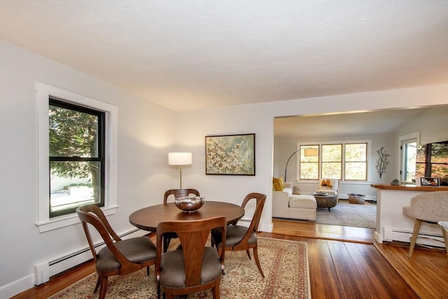 dining space with a baseboard radiator, hardwood / wood-style floors, and baseboards