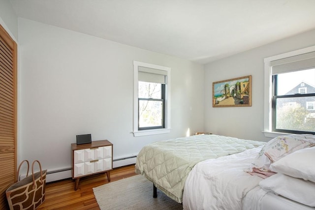 bedroom featuring multiple windows, wood finished floors, baseboard heating, and a closet