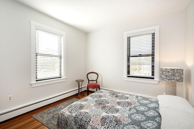 bedroom with a baseboard heating unit, multiple windows, and wood finished floors