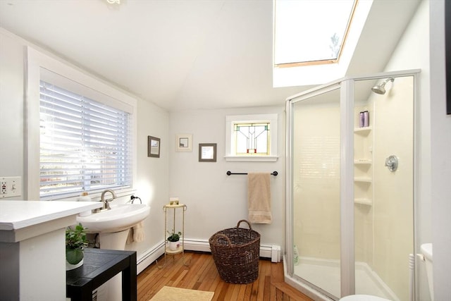 bathroom featuring a skylight, hardwood / wood-style flooring, a baseboard heating unit, healthy amount of natural light, and vaulted ceiling