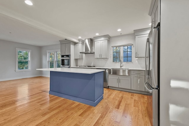 kitchen featuring gray cabinetry, light hardwood / wood-style flooring, wall chimney exhaust hood, appliances with stainless steel finishes, and a kitchen island