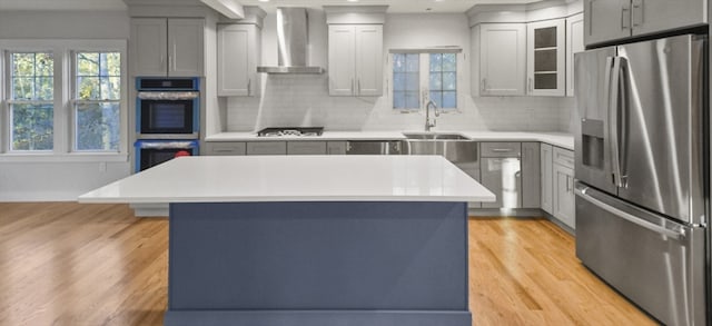 kitchen with a kitchen island, stainless steel appliances, wall chimney range hood, and light wood-type flooring