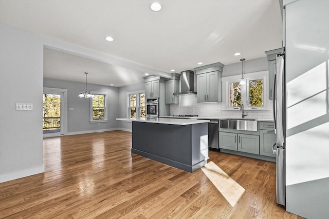 kitchen featuring appliances with stainless steel finishes, sink, wall chimney range hood, light hardwood / wood-style flooring, and a center island