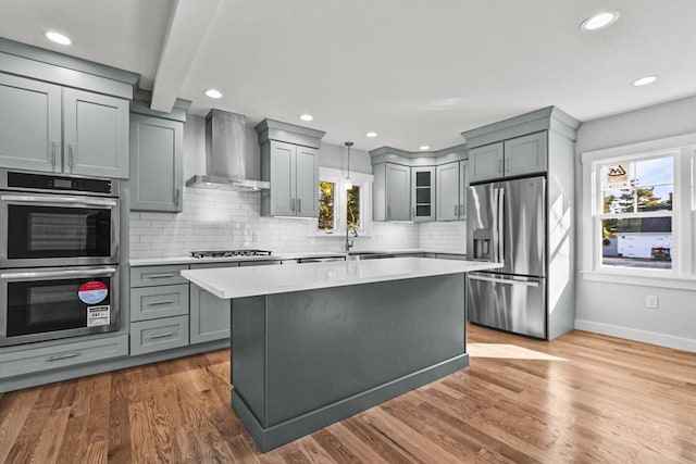 kitchen with tasteful backsplash, wall chimney exhaust hood, stainless steel appliances, decorative light fixtures, and light hardwood / wood-style floors