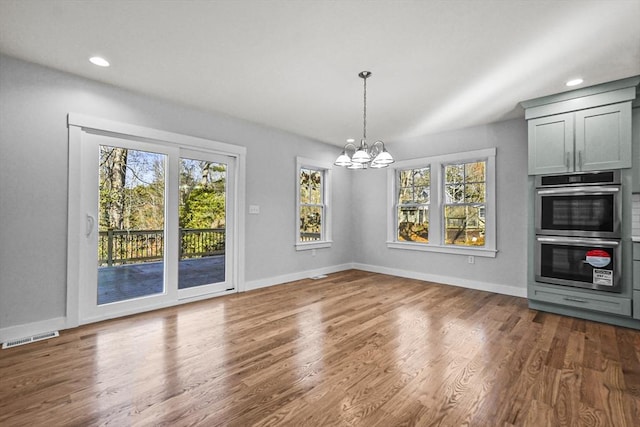 unfurnished dining area featuring dark hardwood / wood-style flooring, a healthy amount of sunlight, and a notable chandelier