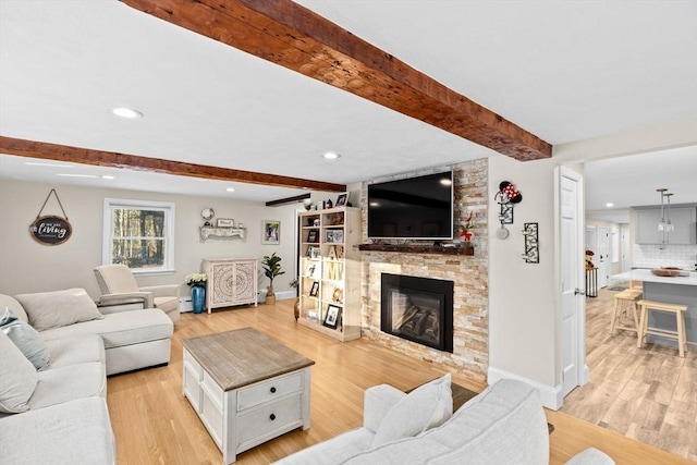 living room featuring beam ceiling, a stone fireplace, and light hardwood / wood-style flooring